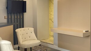 A hotel room with a bed, a chair, a small table, a TV mounted on the wall, and a shower area. - Panula Park Hotel (Izmir)