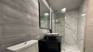 A bathroom with a marble floor, a black vanity, a white toilet, and a mirror above the vanity. - Panula Park Hotel (Izmir)