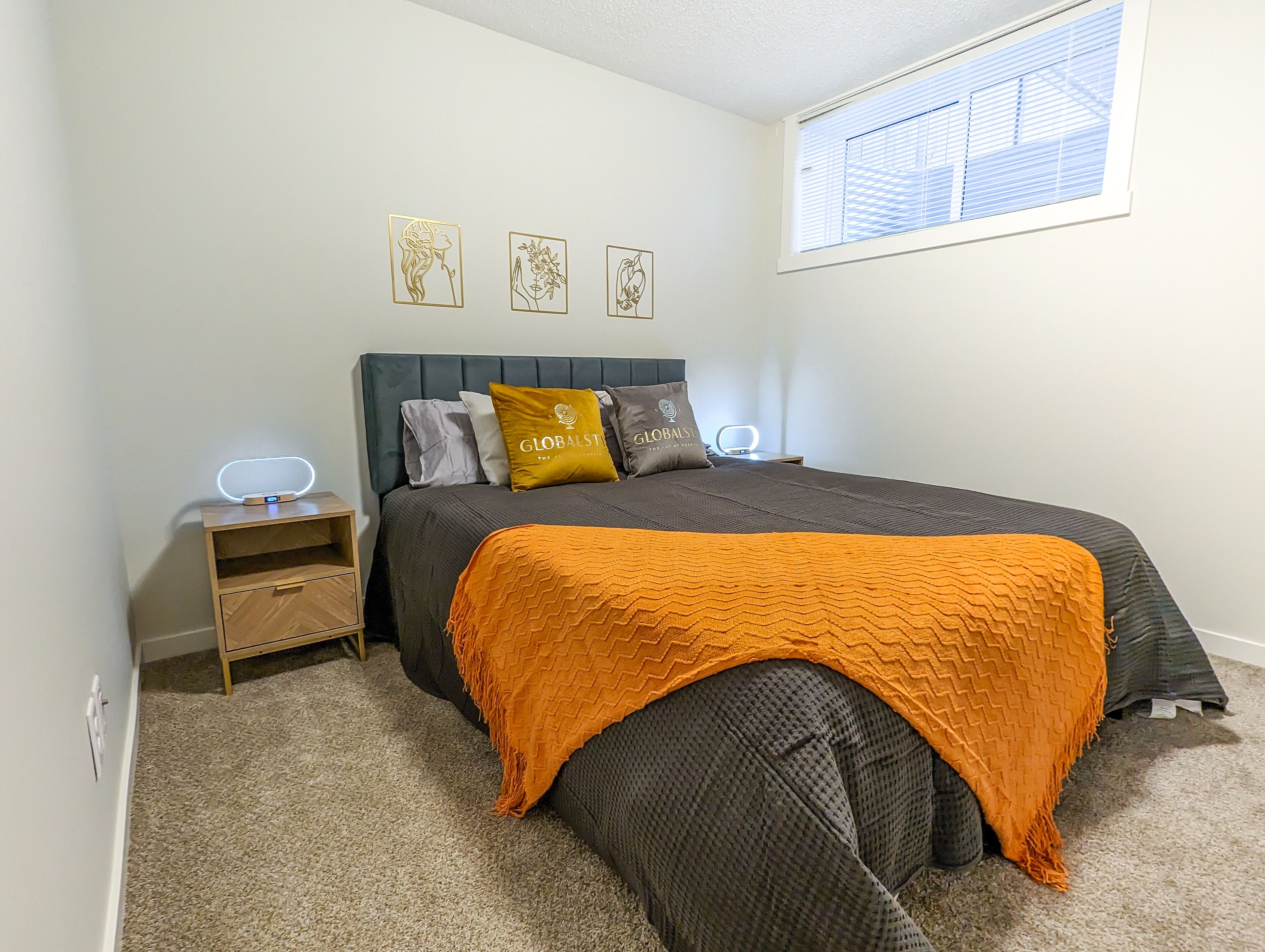 A bedroom with a bed, a nightstand, a lamp, and a window with blinds.