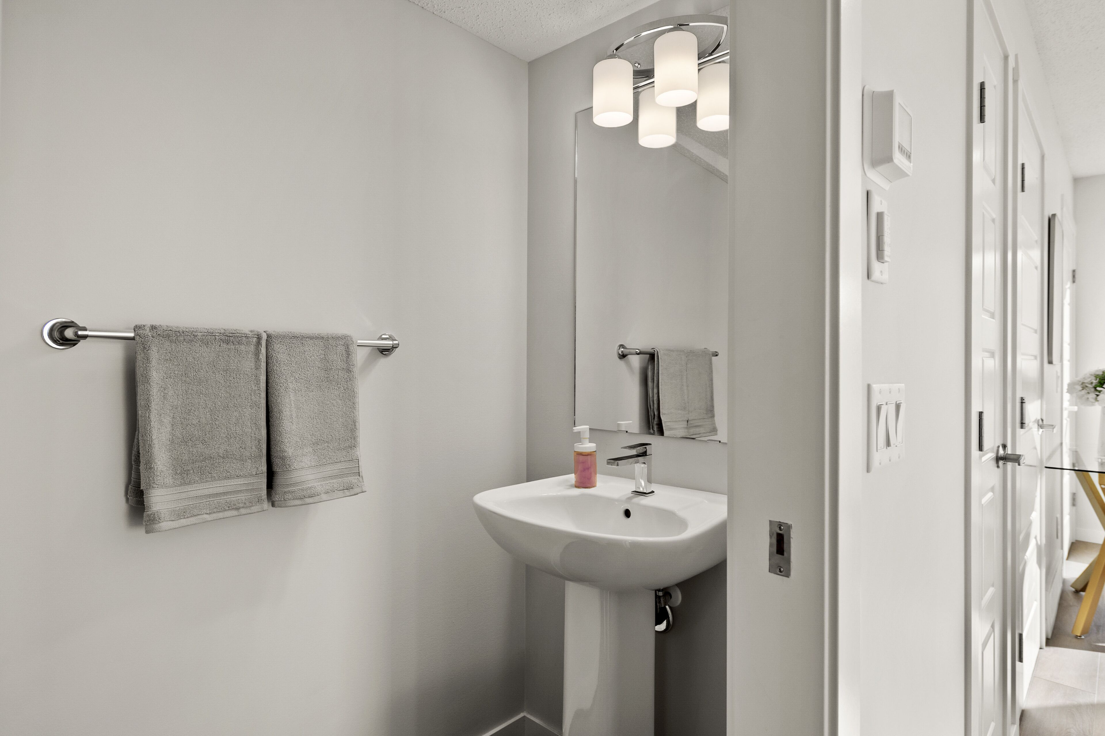 A bathroom with a white sink, a towel rack with two towels, a mirror, and a light fixture above the mirror.