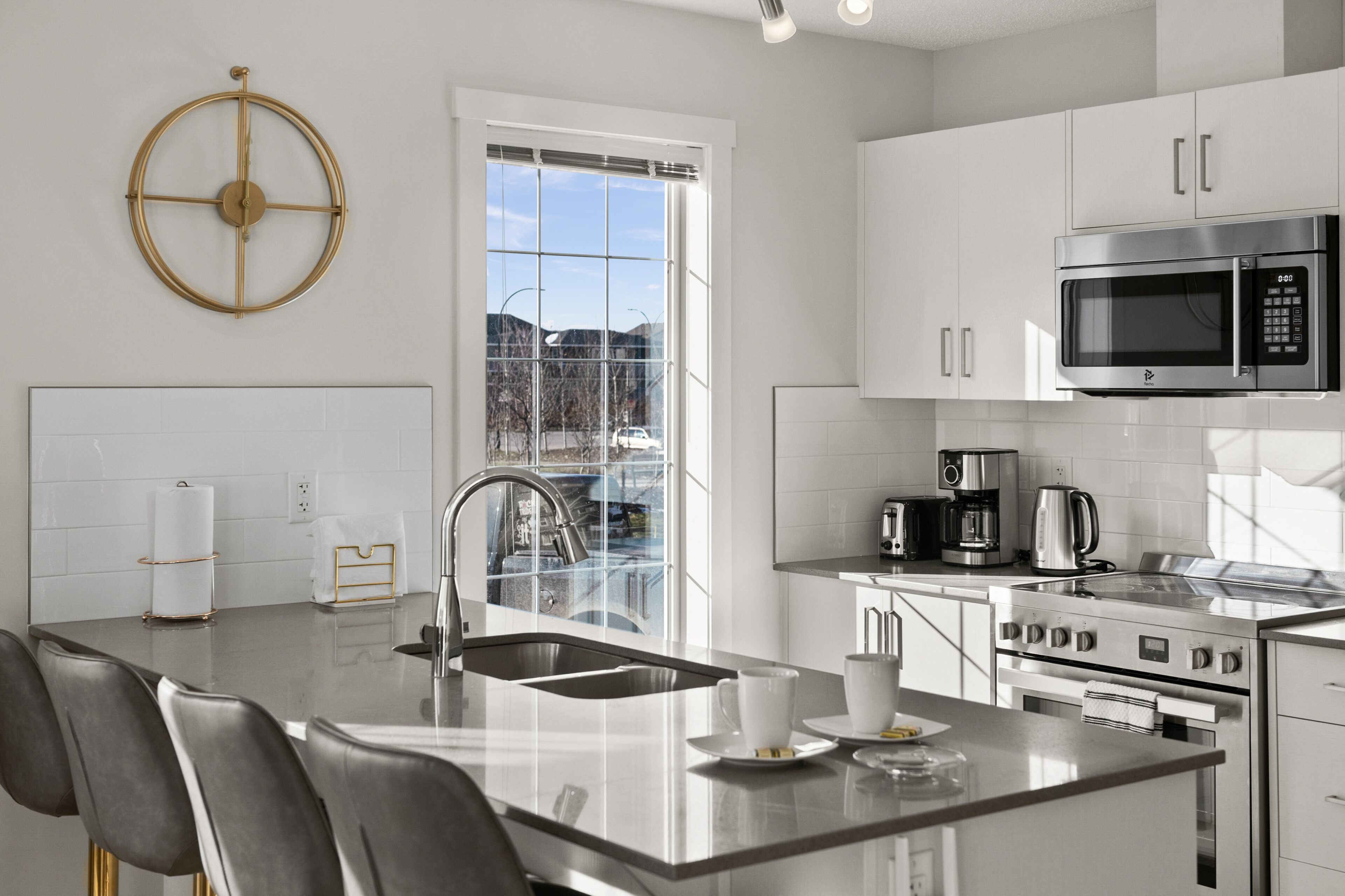 A modern kitchen with a central island, stainless steel appliances, and a large window providing a view of the outdoors.