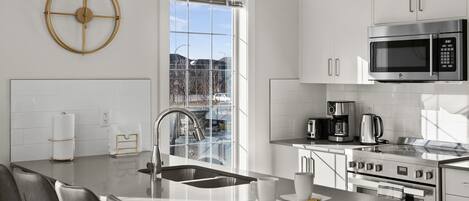 A modern kitchen with a central island, stainless steel appliances, and a large window providing a view of the outdoors.