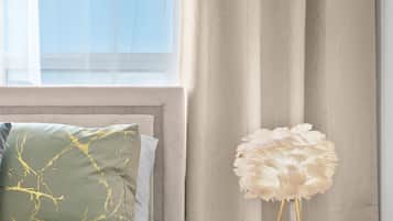 Ein Schlafzimmer mit einem Bett, einem runden Nachttisch mit einer weißen Lampe und einem Fenster mit Vorhängen.