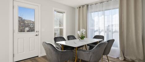 A dining area with a white table, six grey chairs, and a vase of white flowers.
