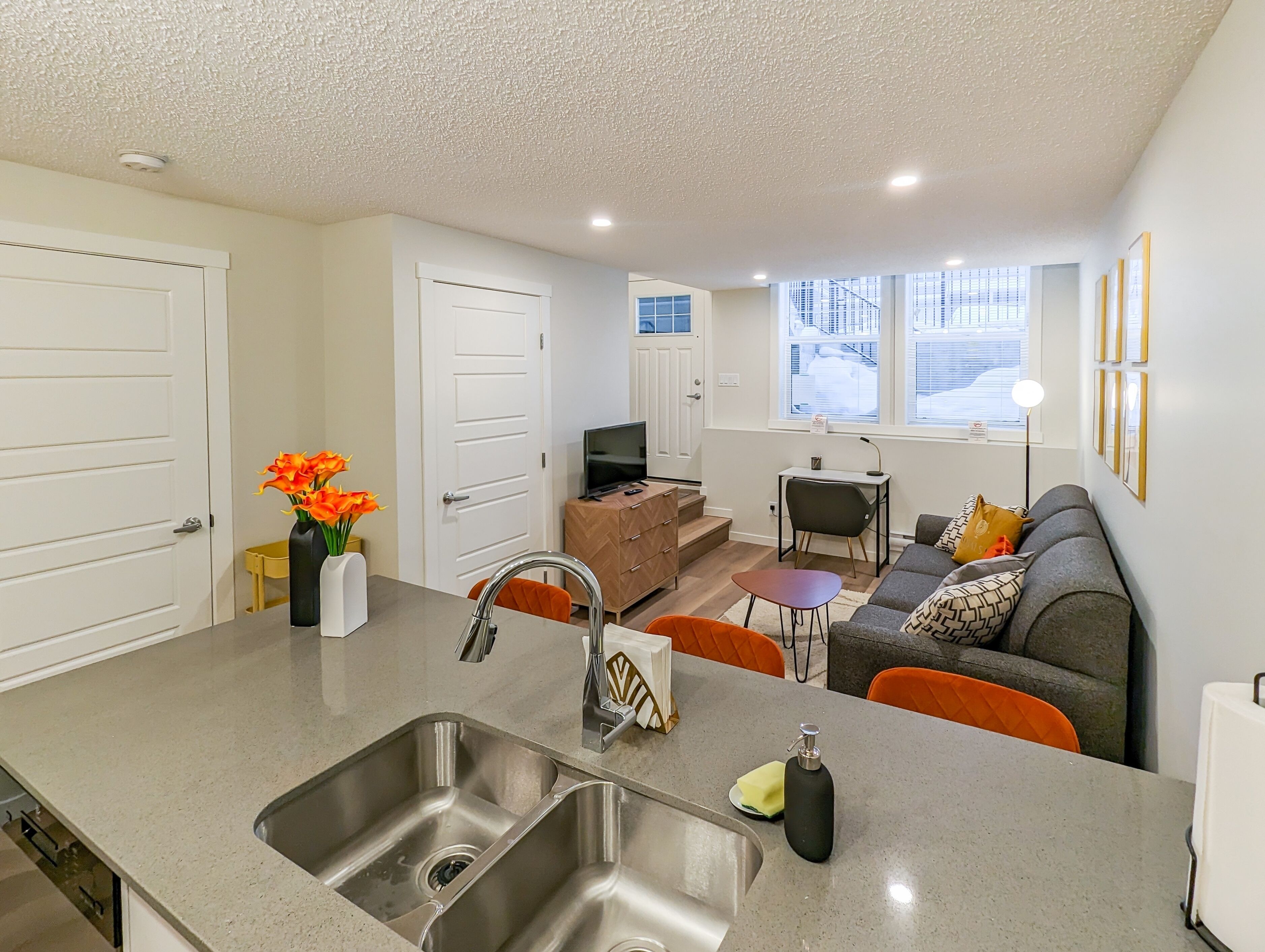 A modern kitchen with a sink, a dining area with a table and chairs, a sofa, and a TV.