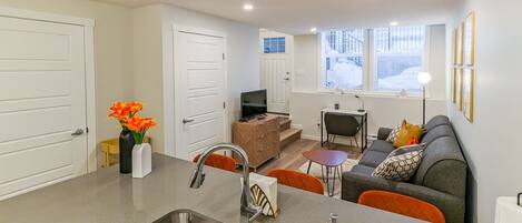 A modern kitchen with a sink, a dining area with a table and chairs, a sofa, and a TV.