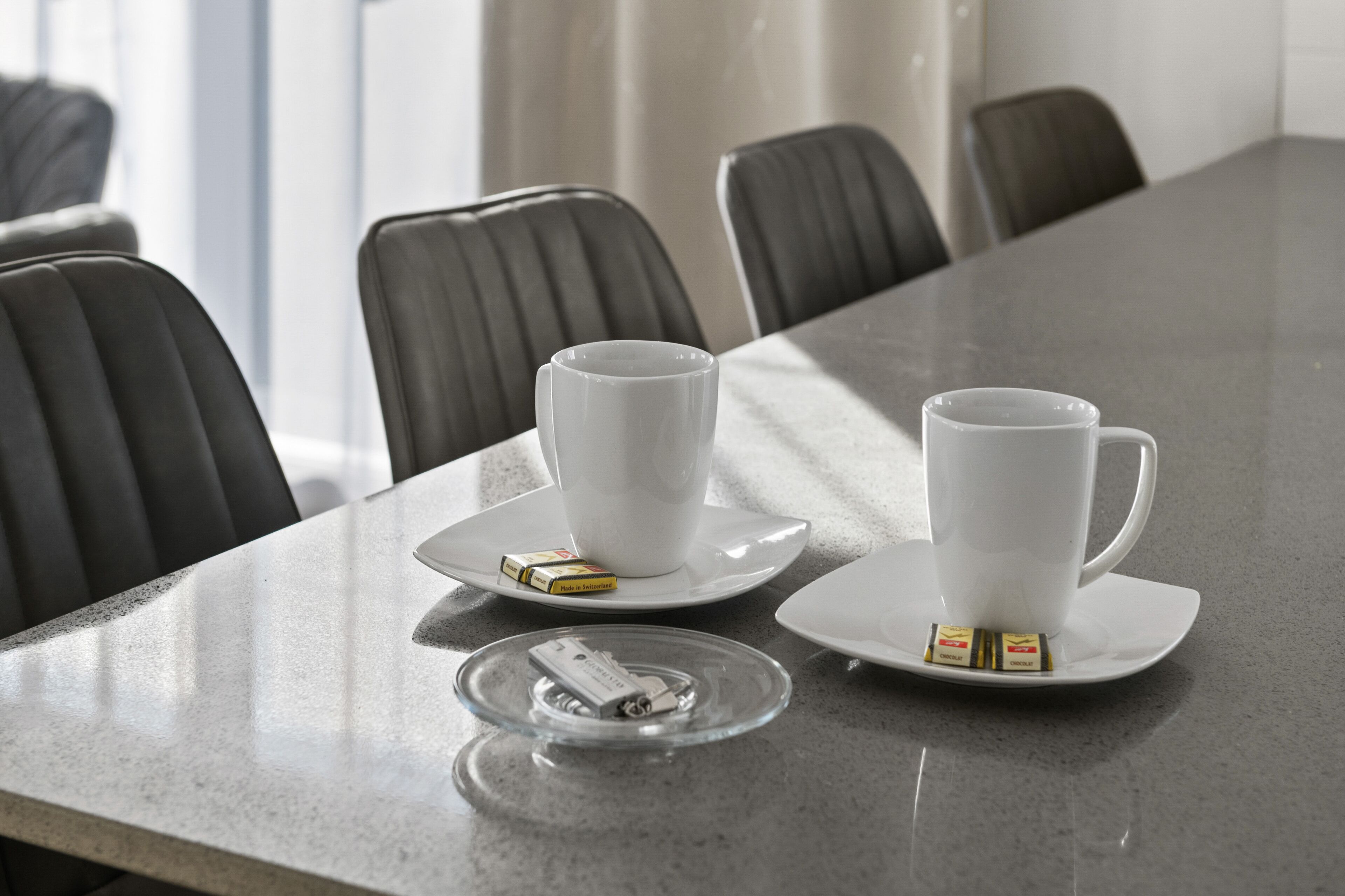 A conference table with two white cups and saucers, a pack of tissues, and a lighter.
