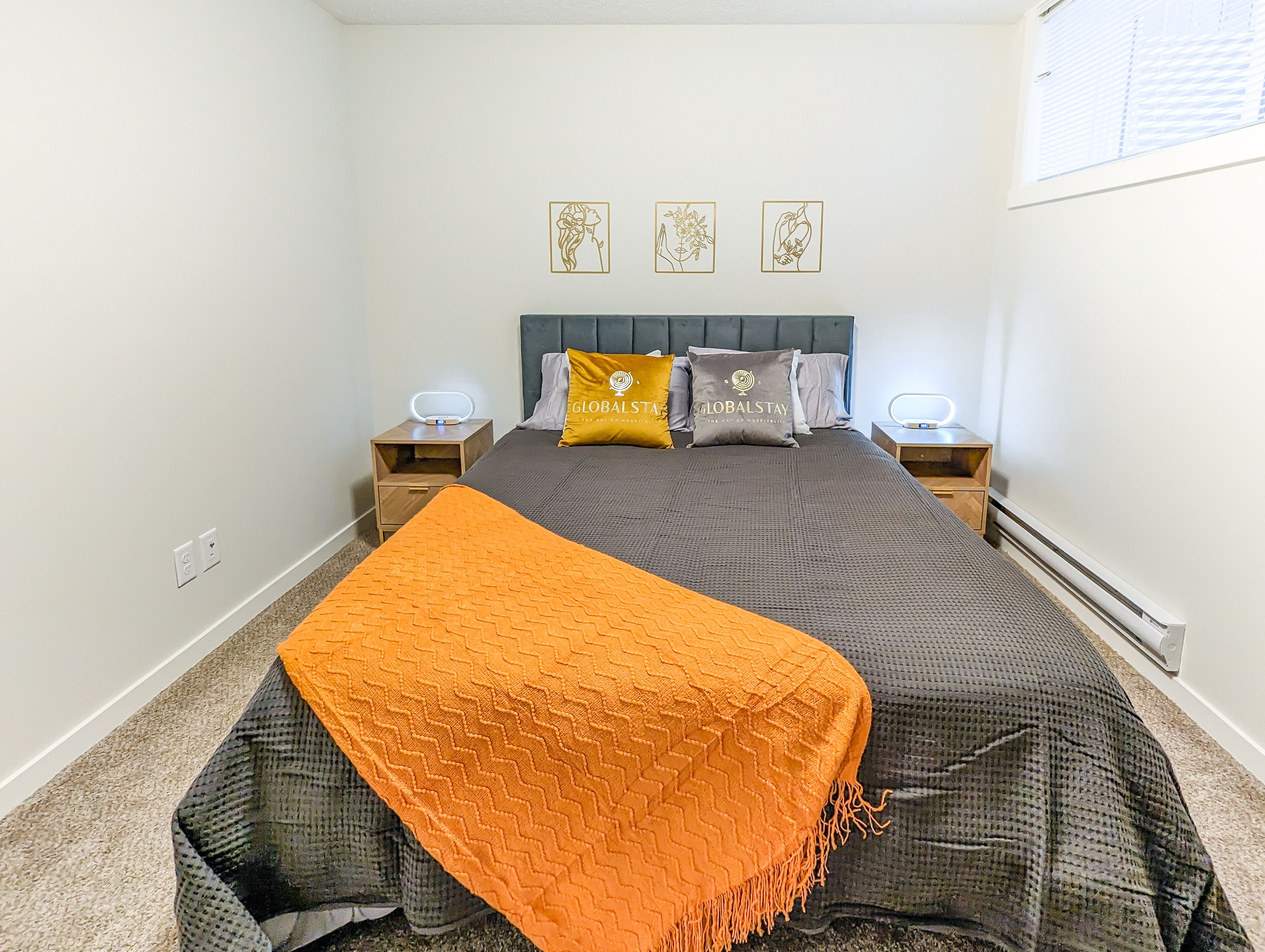 A bedroom with a bed, two bedside tables, a nightstand, a blanket, and three wall art pieces.