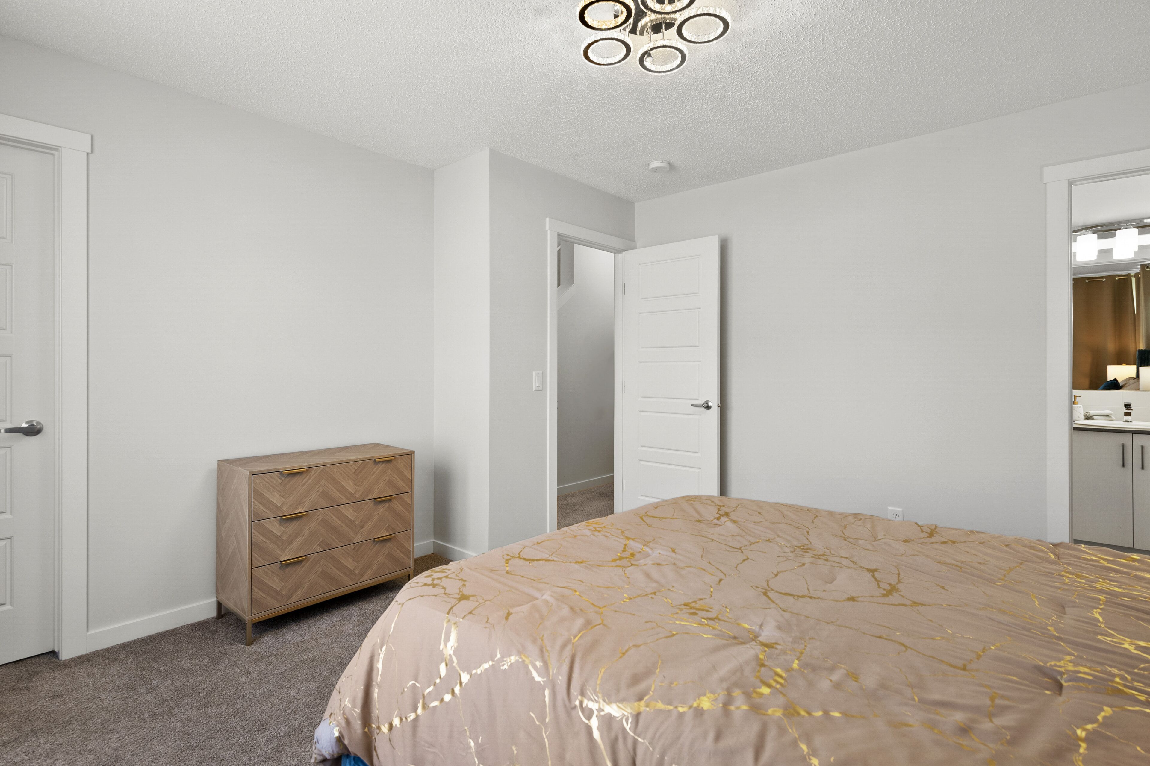 A bedroom with a bed, dresser, and a door leading to another room.