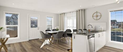 A modern kitchen with a central island, white cabinetry, and a dining area with grey chairs.