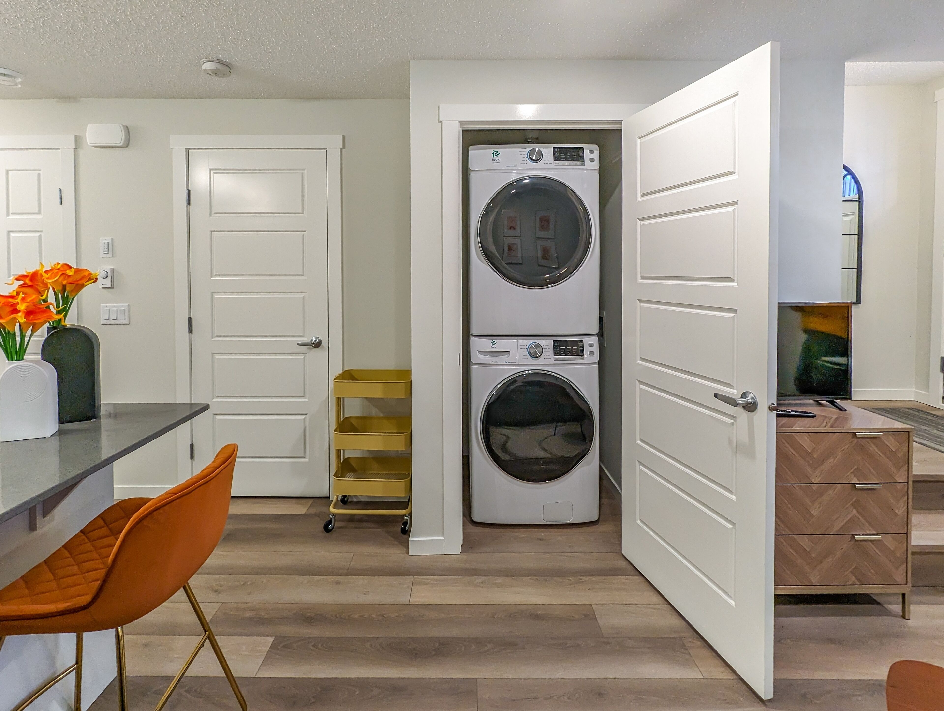 A laundry room with two stacked front-loading washers and dryers, a small cart, and a wooden herringbone cabinet.