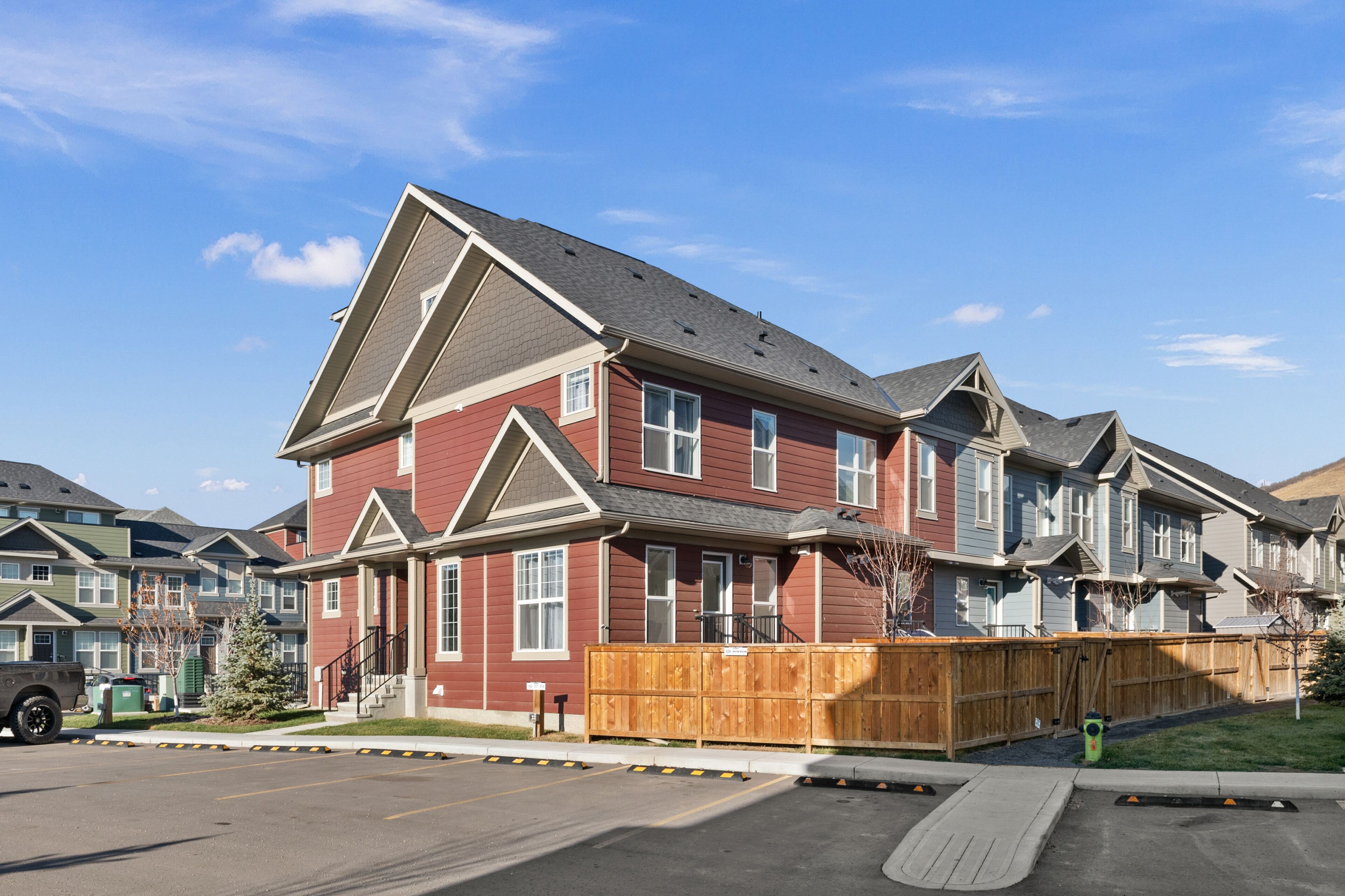 A multi-story residential building with a red exterior, a wooden fence, and a clear blue sky.