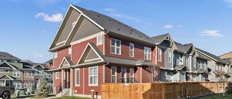 A multi-story residential building with a red exterior, a wooden fence, and a clear blue sky.