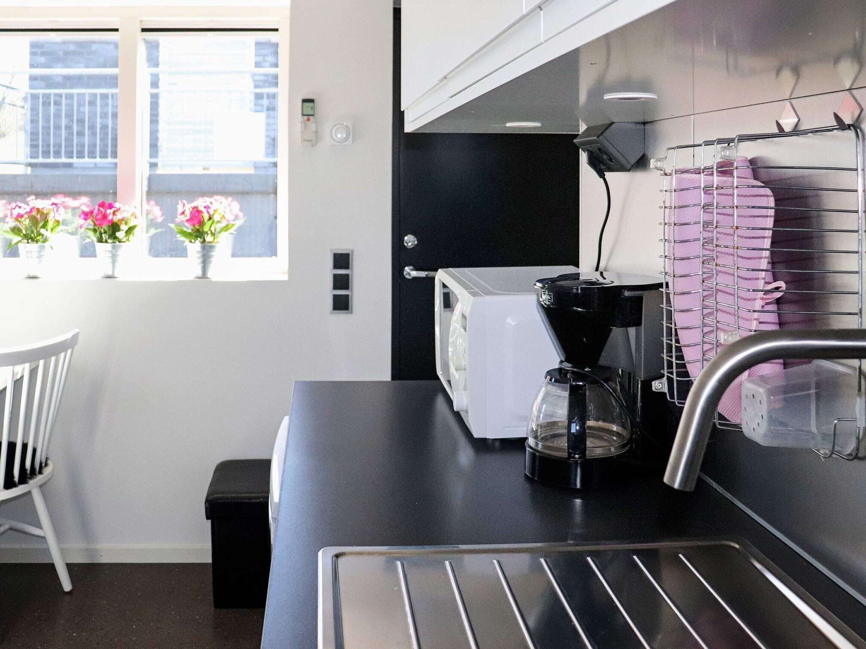 A modern kitchen with a coffee maker, a toaster, and a sink. There are potted plants on the windowsill.
