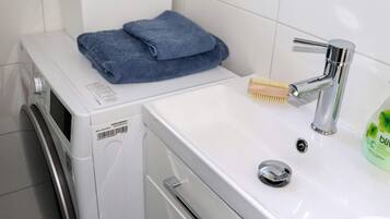 Una lavadora con una toalla azul doblada encima, un cepillo de madera y una botella de detergue líquido sobre un lavabo blanco.