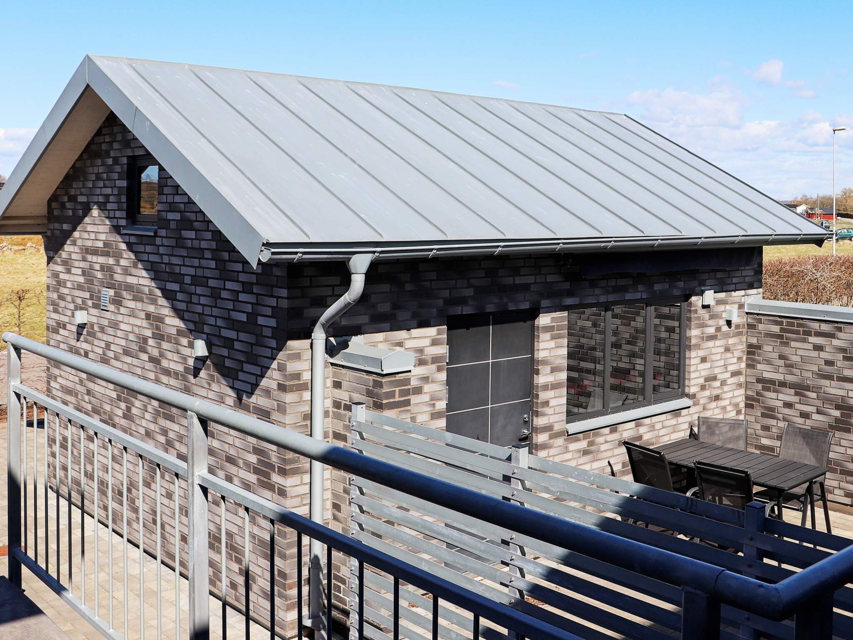 A small building with a metal roof and brick walls, featuring a covered outdoor seating area with tables and chairs.
