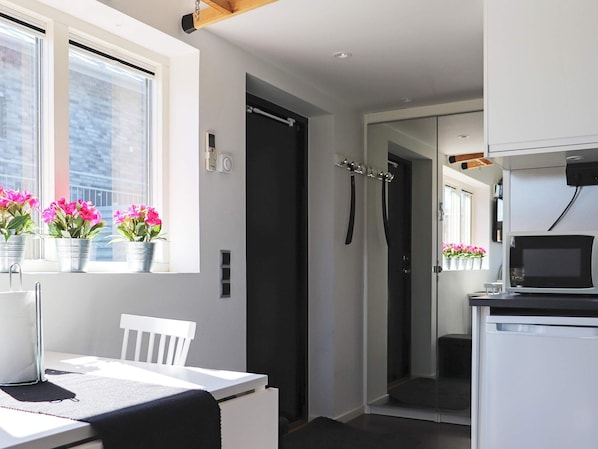 A modern kitchen with a microwave, a white table with a chair, and potted plants on the windowsill. - 4 Star Holiday Home in Varberg (Varberg)