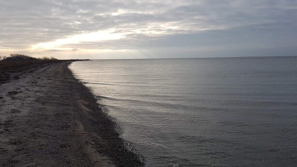 En strand med en sti af sand, der fører ned til vandet, under en overskyet himmel.
