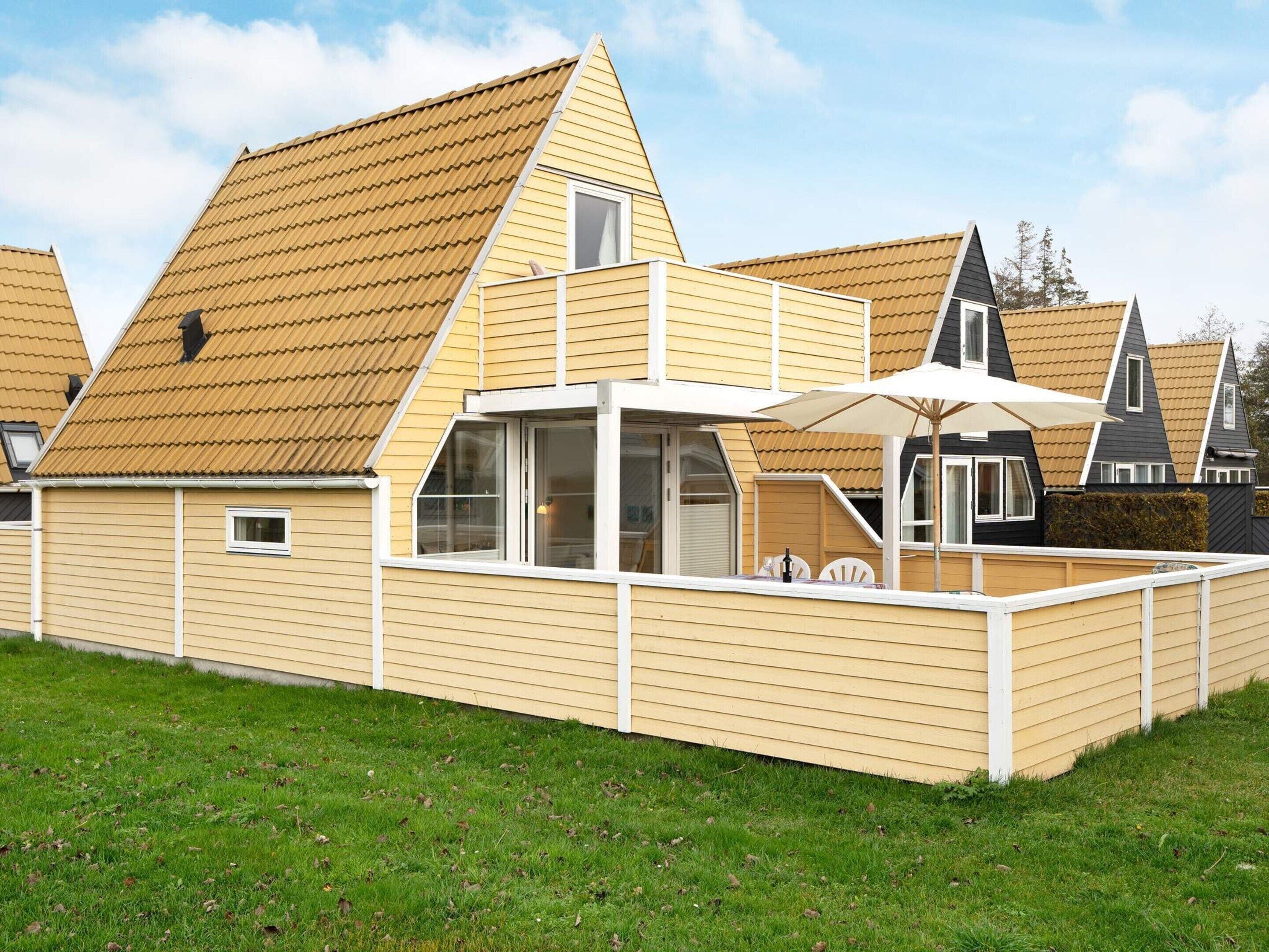 A modern house with a sloped roof, a balcony with a white umbrella, and a small window.