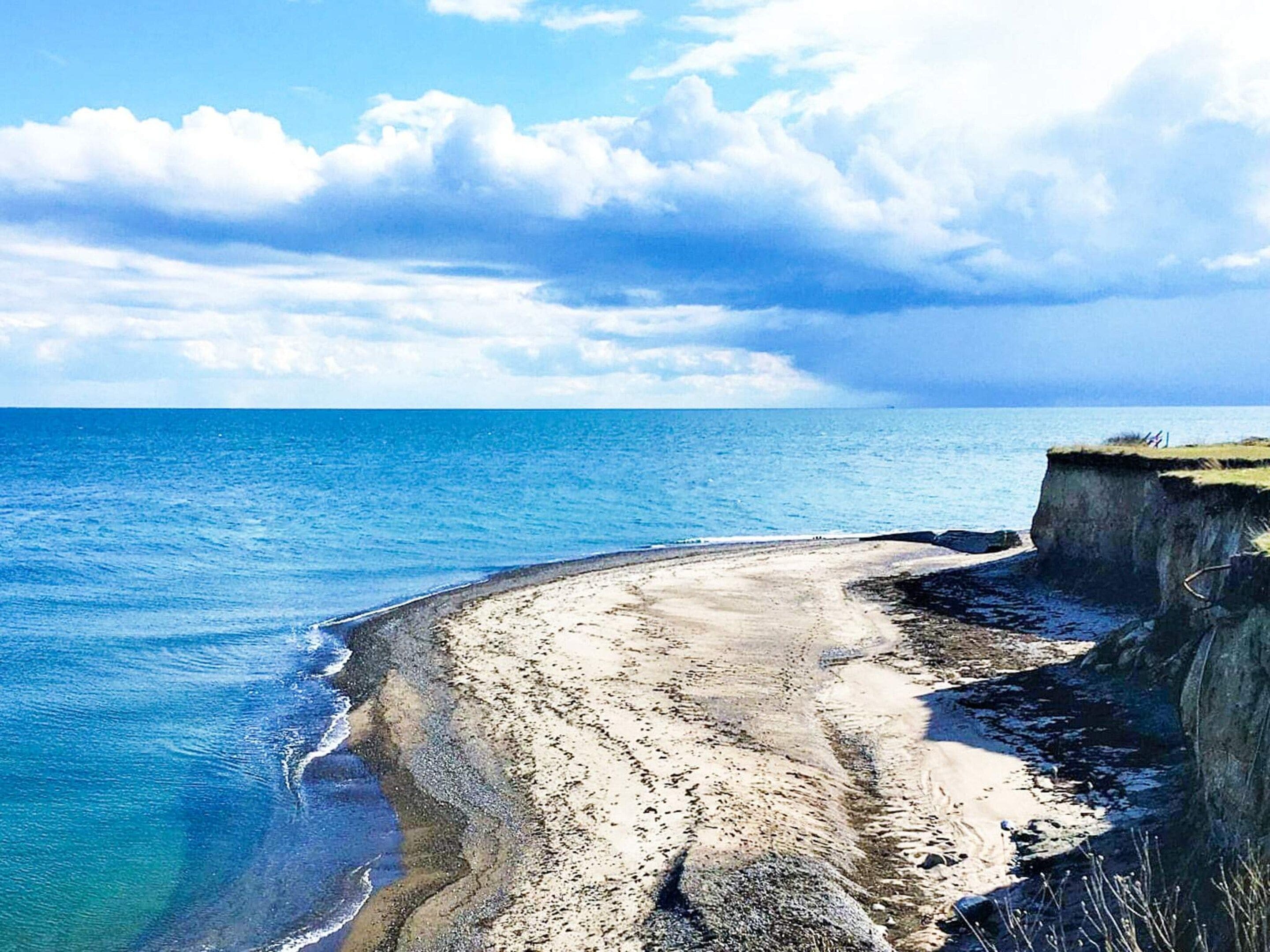 Un paisaje costero con una playa arenosa, un acantilado y el océano.