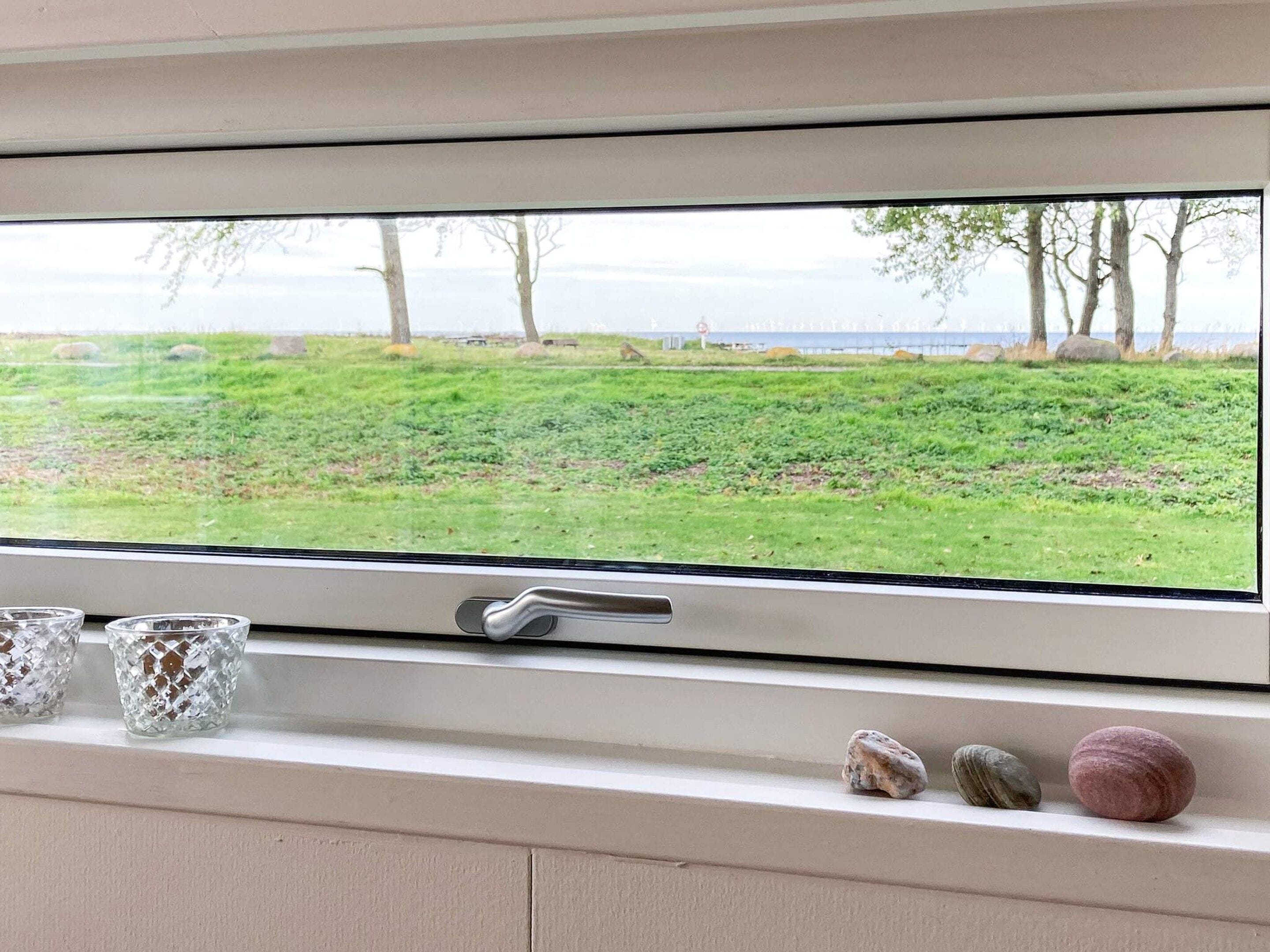 Janela com vista para um campo gramado e árvores, uma maçaneta e três objetos decorativos no parapeito.