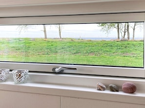 A window with a view of a grassy field and trees, a door handle, and three decorative items on the sill. - 4 Person Holiday Home in Gedser (Gedser)