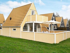 A modern house with a sloped roof, a balcony with a table and chairs, and a large umbrella. - 4 Person Holiday Home in Gedser (Gedser)