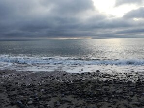 A beach with waves, pebbles, and a cloudy sky.
