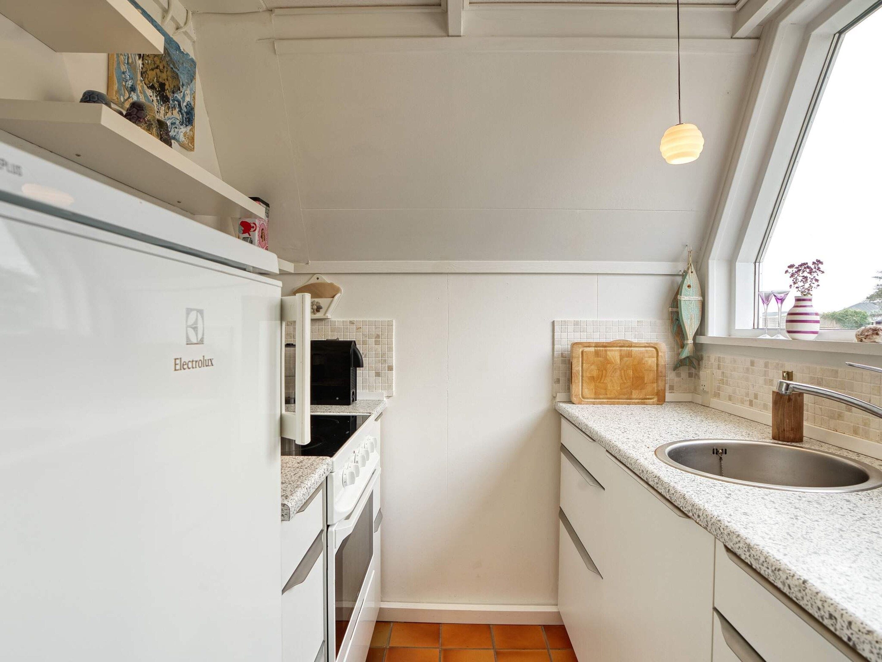 A compact kitchen with a white refrigerator, a stove, a sink, and a window with a view.