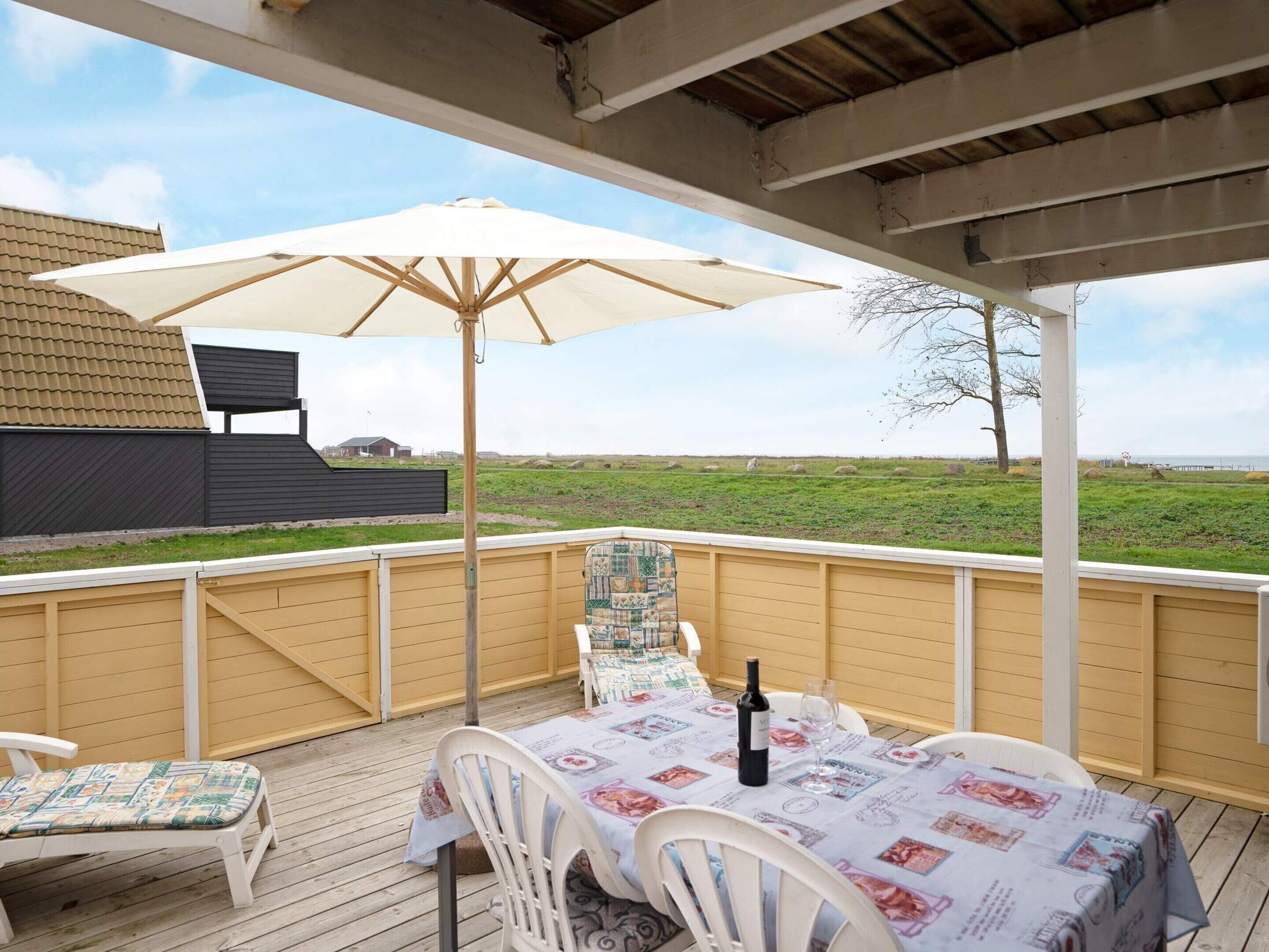 Un patio exterior techado con una mesa preparada para dos, una sombrilla y vistas a un campo cubierto de césped.