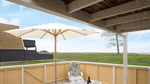 En overdækket terrasse med et bord til to, en parasol og udsigt over en græsplæne.