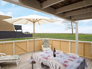 A covered outdoor patio with a table set for two, an umbrella, and a view of a grassy field. - 4 Person Holiday Home in Gedser (Gedser)