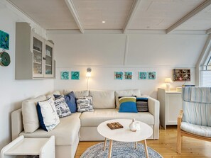 A living room with a sofa, a coffee table, a side table, and a chair. There are wall-mounted shelves with decorative items and a lamp.