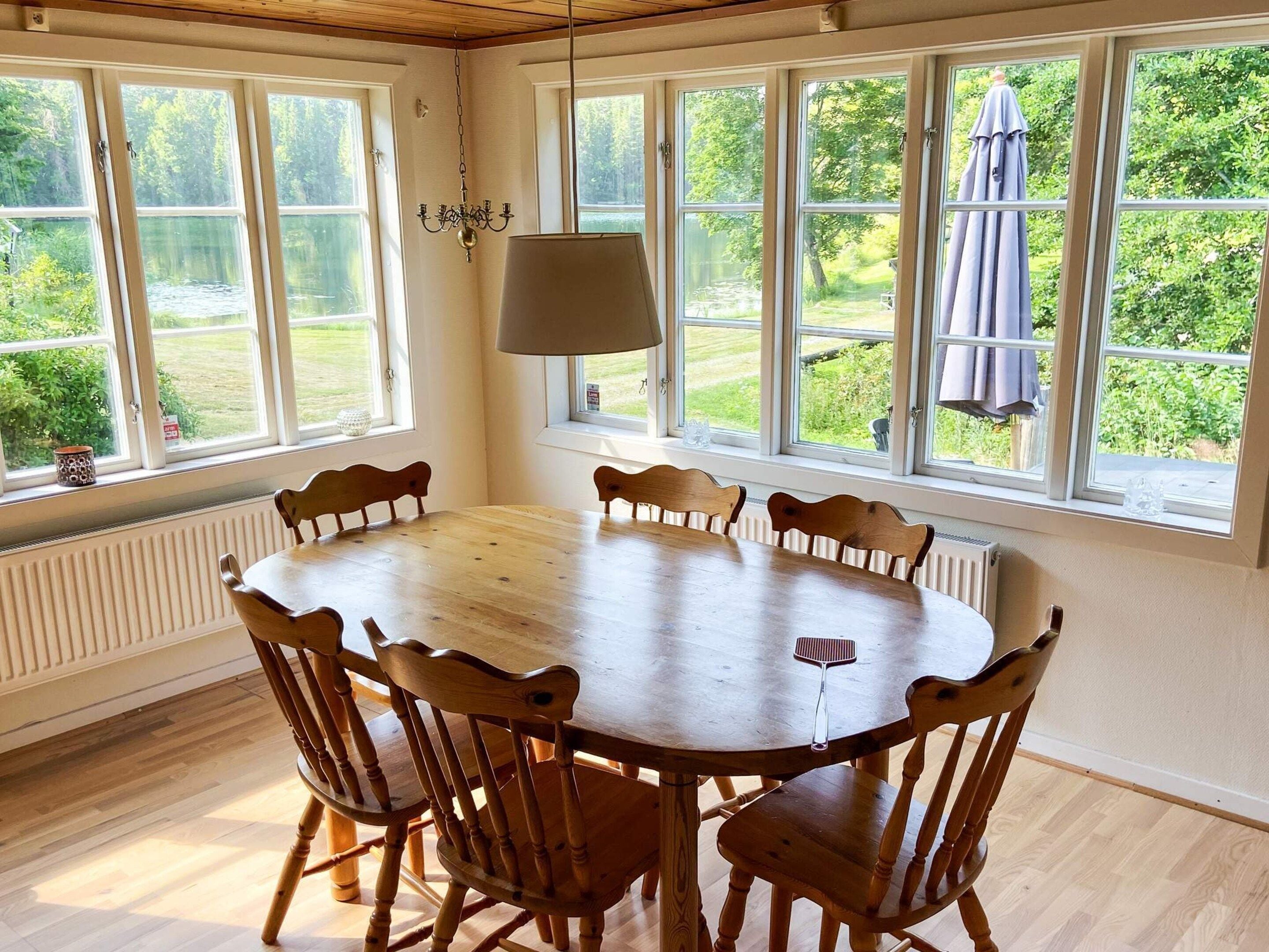 Comedor con mesa redonda de madera y seis sillas, ventanas amplias con vista a zonas verdes y una lámpara colgante.