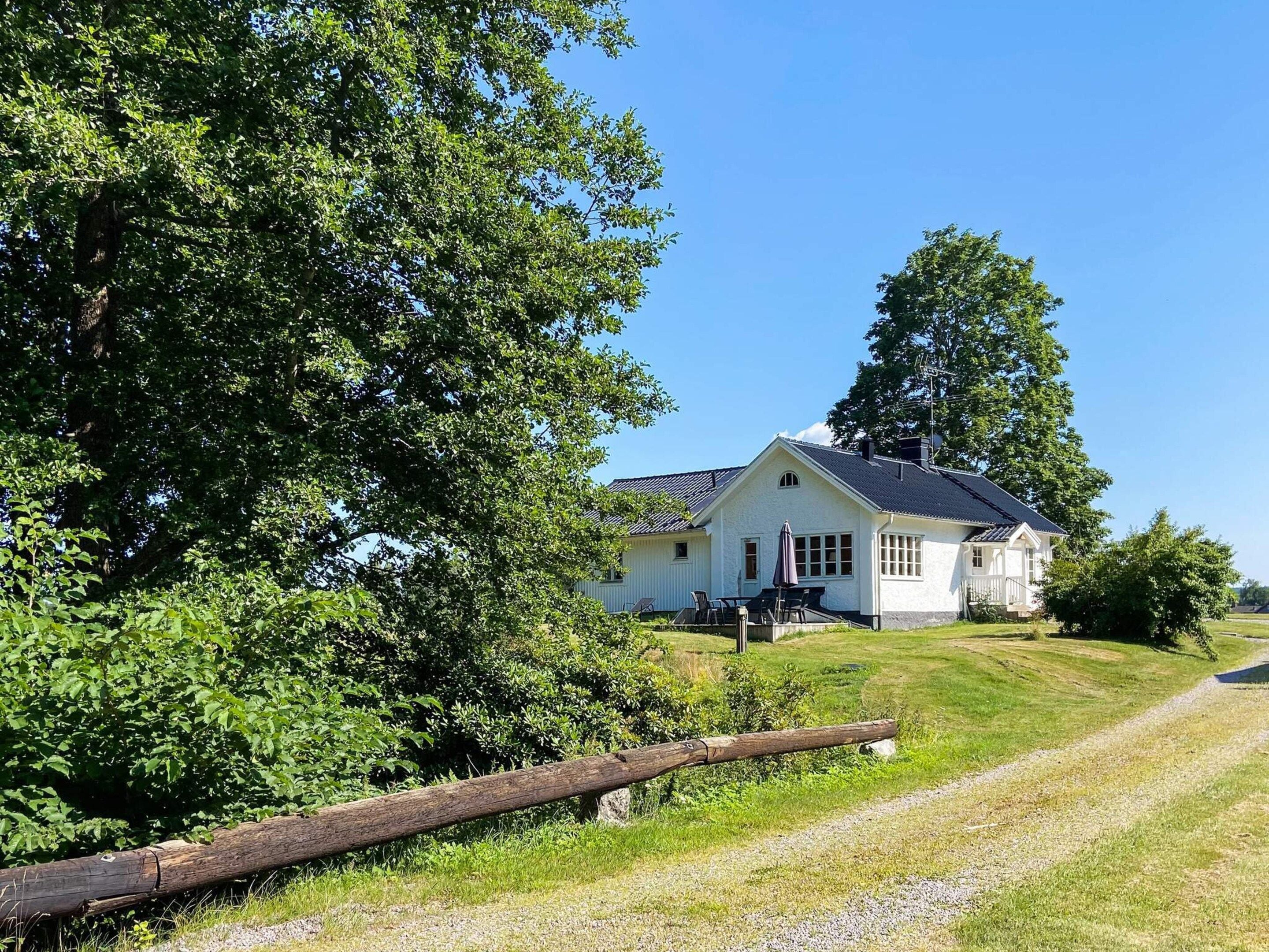 Een wit huis met schuine dak, een veranda met stoelen, en een grindpad er naartoe.
