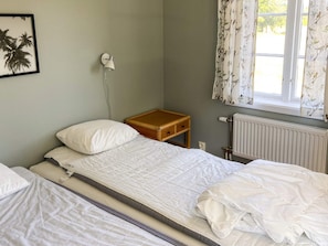 A single bed with a wooden nightstand, a wall-mounted lamp, and a window with curtains. - 5 Star Holiday Home in Asbro (Asbro)