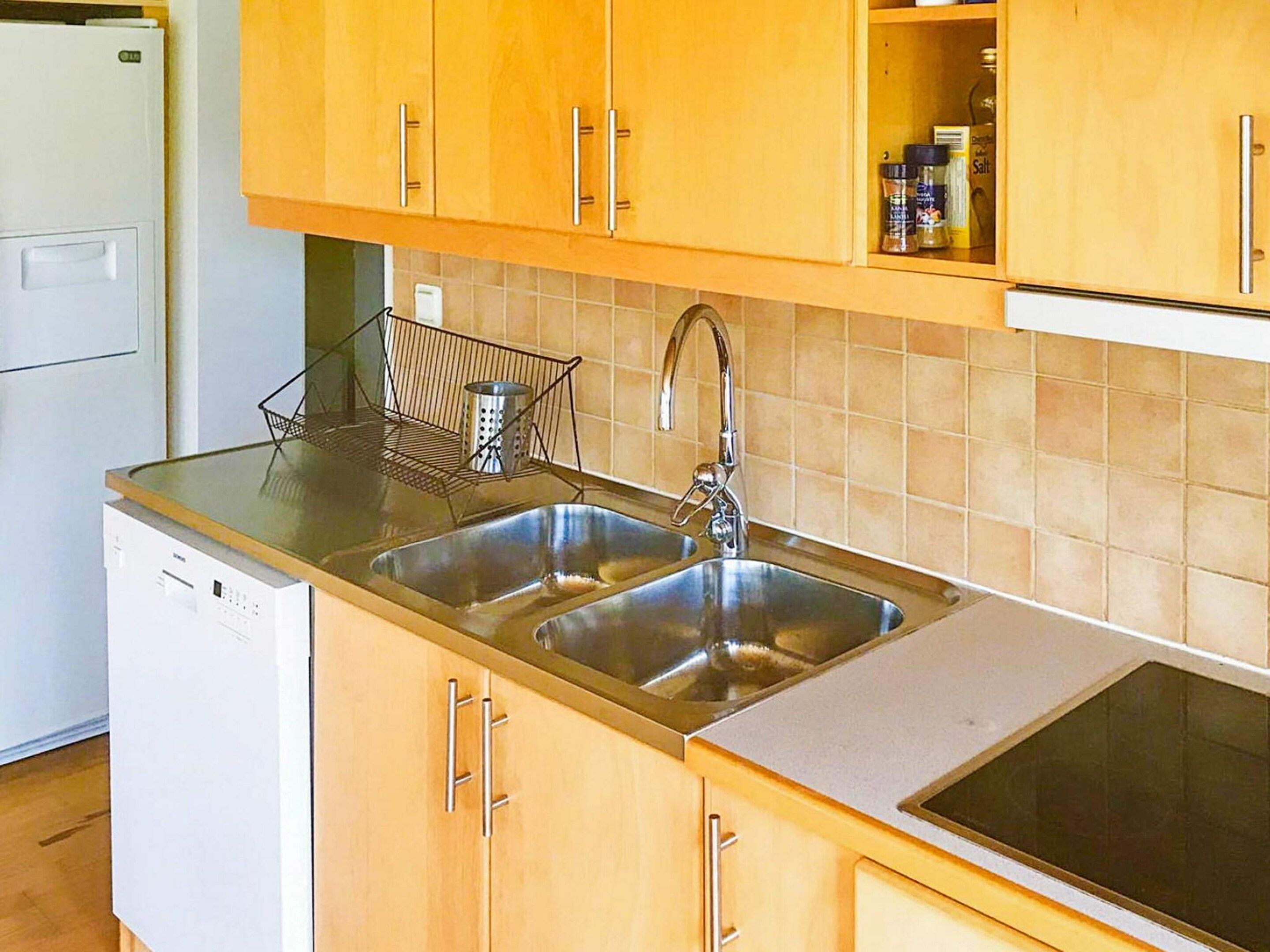 A kitchen with two stainless steel sinks, wooden cabinets, a dish rack, and a built-in oven.
