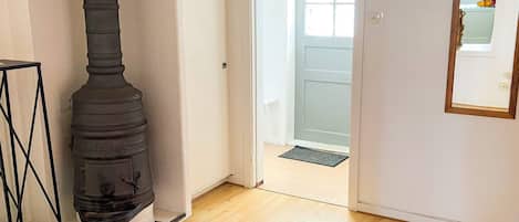 Um quarto com lareira a lenha, um tapete vermelho e uma porta que dá para outro cômodo.