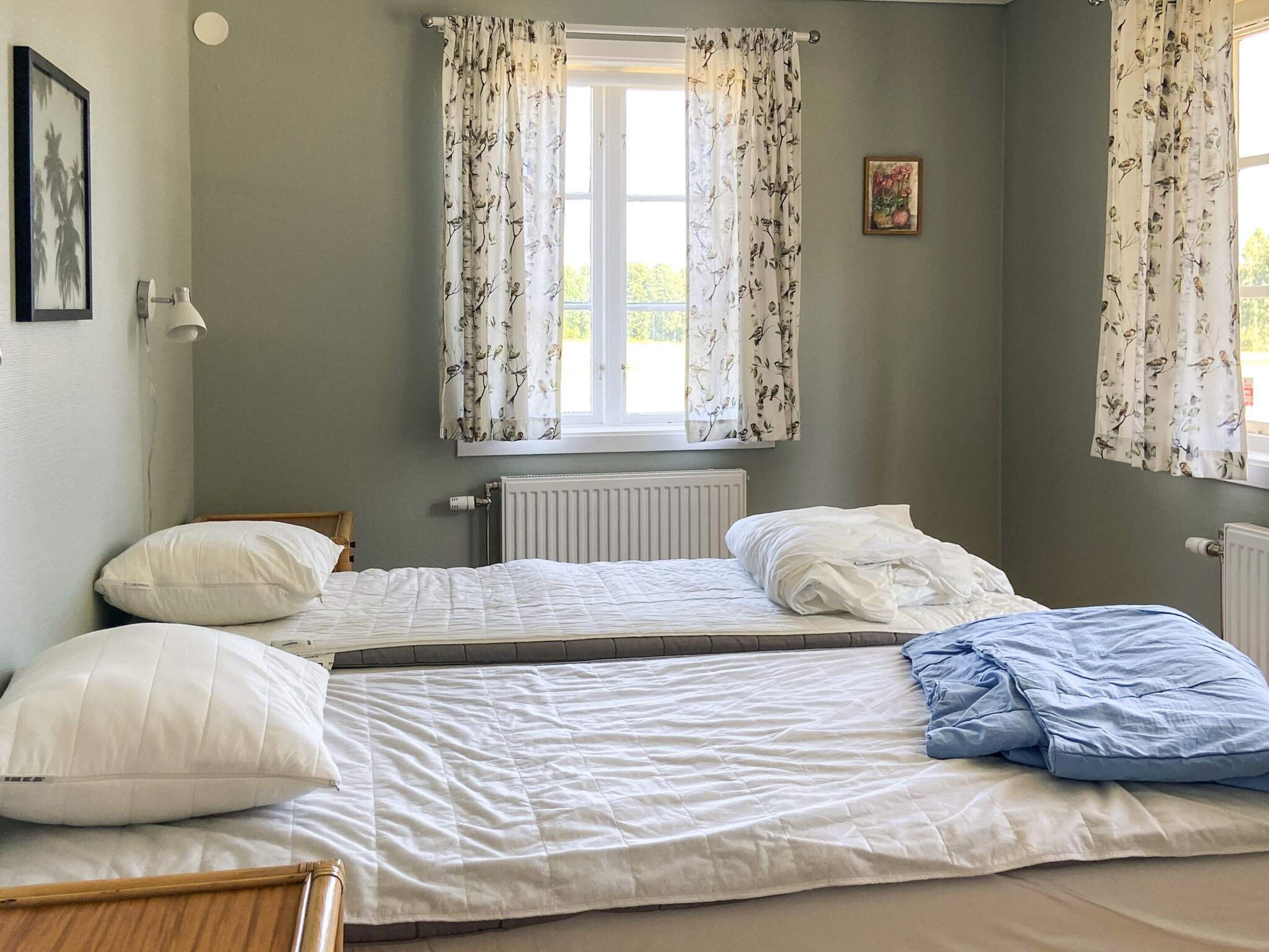 Un dormitorio con dos camas, una ventana con cortinas, un radiador y un cuadro enmarcado en la pared.