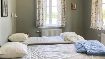 A bedroom with two single beds, a radiator, a window with floral curtains, and a framed picture on the wall.