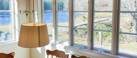 A dining area with a table and chairs, large windows with a view of a lake and trees, and a hanging lamp.