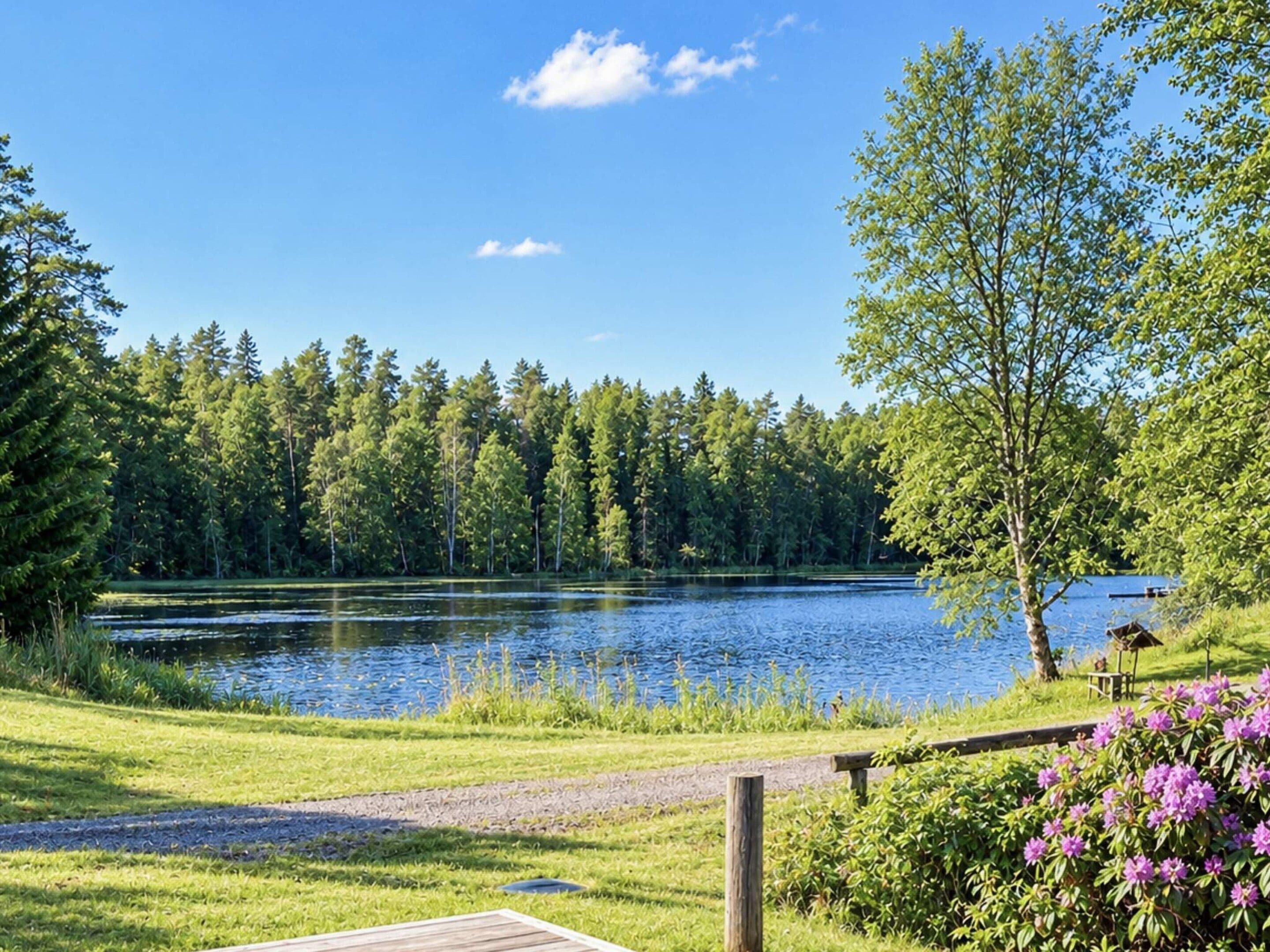 A lakeside view with a wooden deck, a grassy area, and a forest in the background.