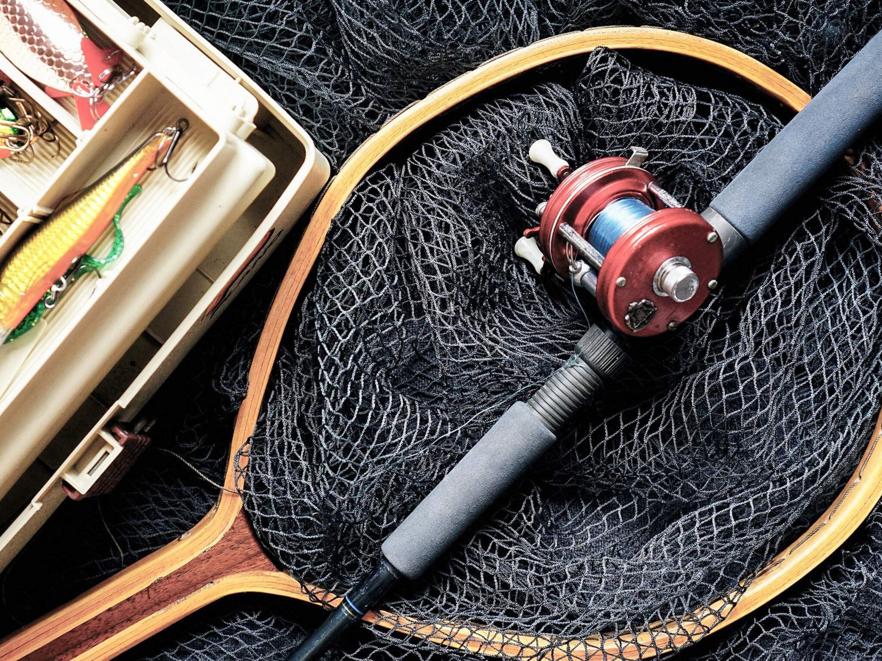 Carrete de pesca y caja de aparejos sobre una superficie de madera, con redes de pesca.