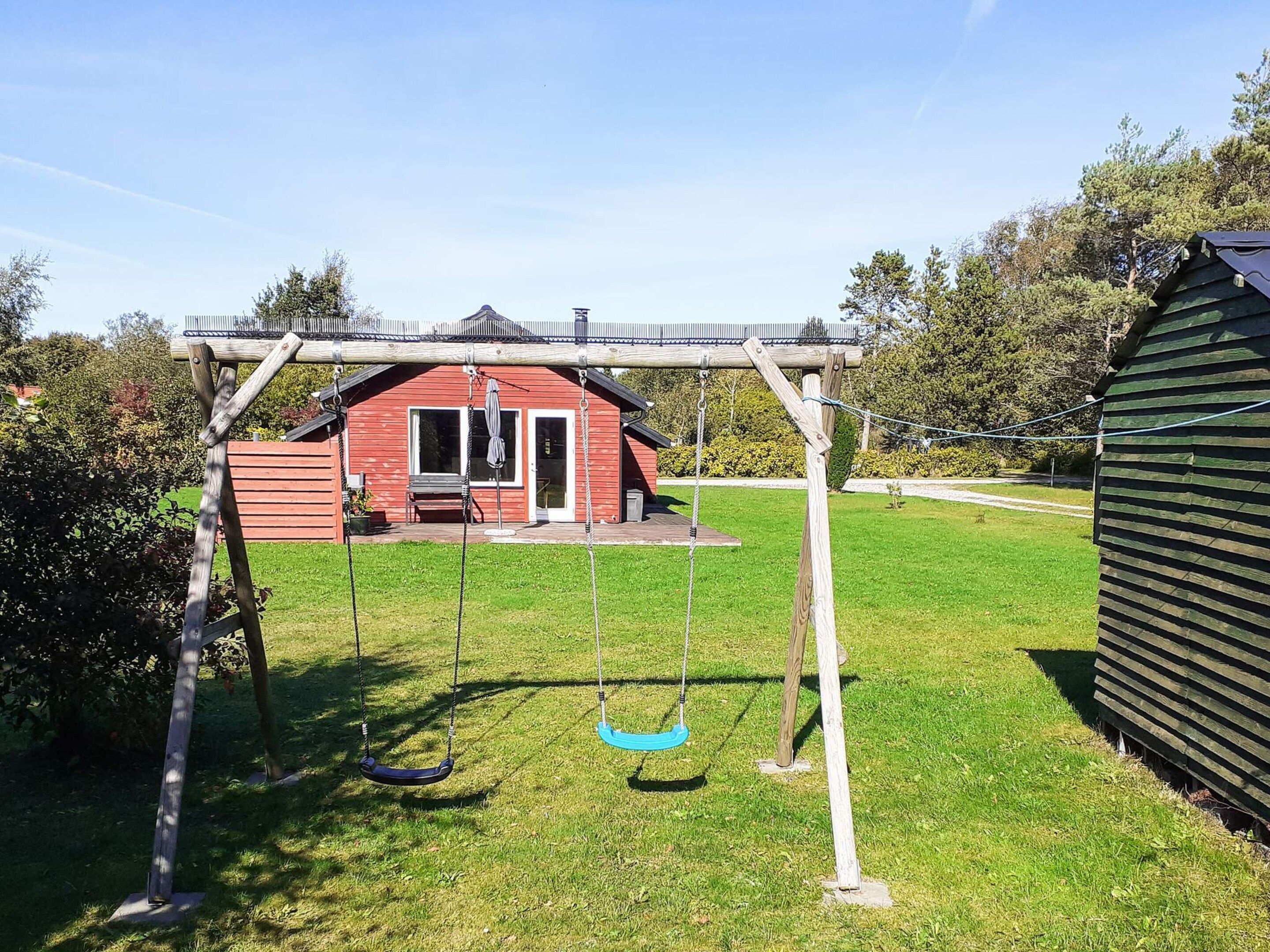 A wooden swing set in a backyard with a red house in the background.