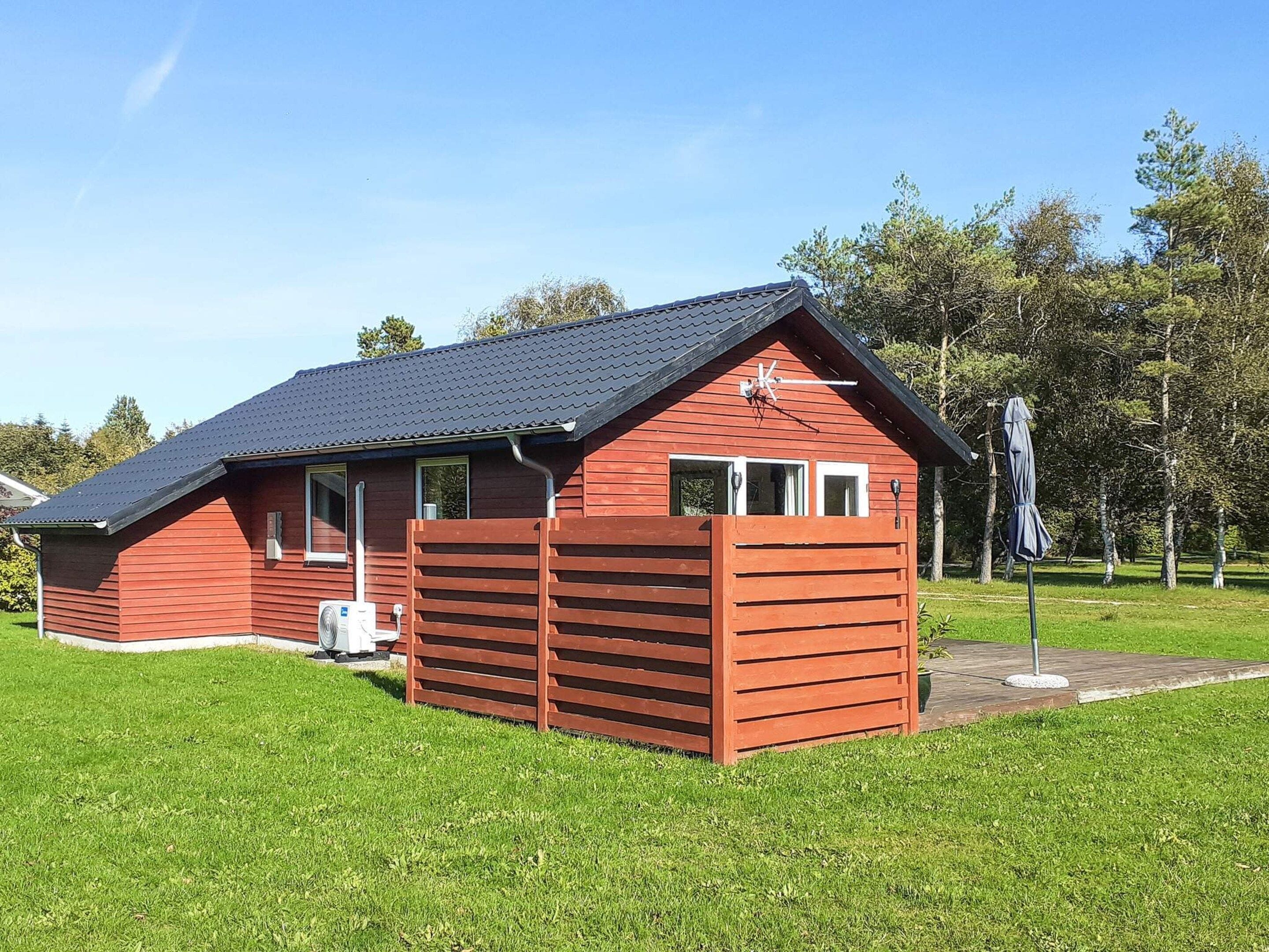 Eine rote Holzhütte mit geneigtem Dach, einer kleinen Veranda und einem Fenster.