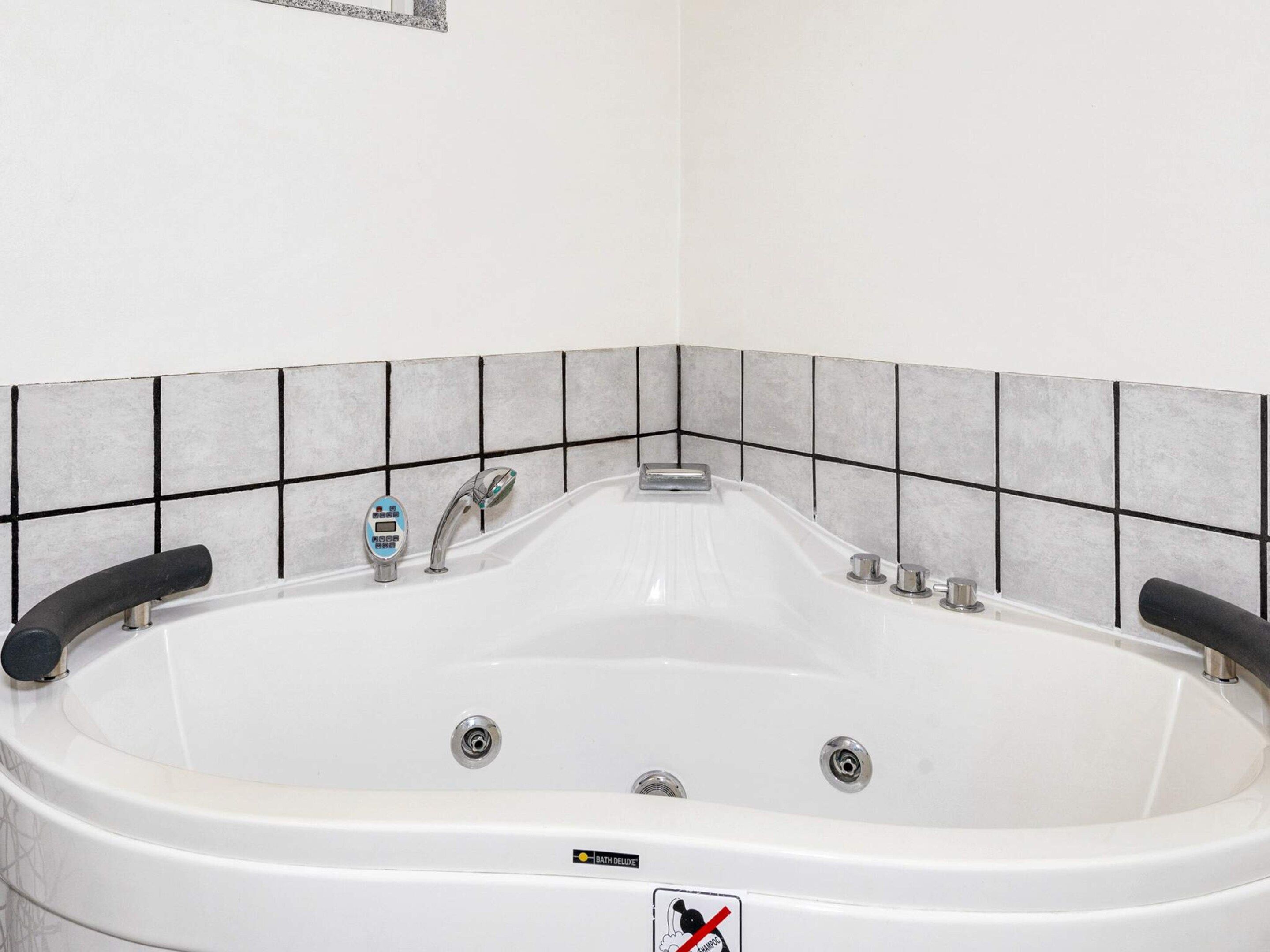 Una bañera blanca con panel de control, dos llaves y desagüe.