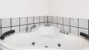 Una bañera blanca con panel de control, dos llaves y desagüe.