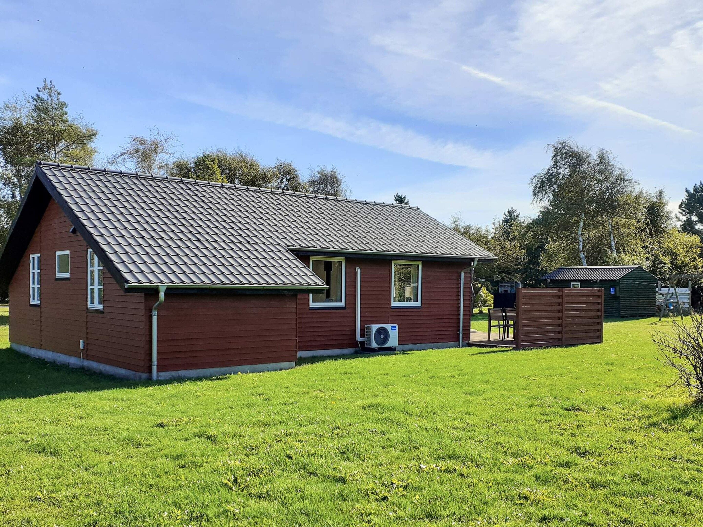 A single-story wooden house with a sloped roof, a small attached shed, and a grassy yard.