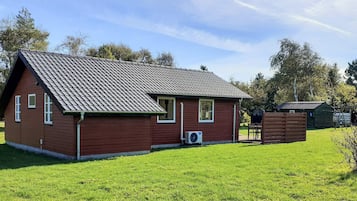 Una casa roja de madera con techo de tejas, un cobertizo pequeño adosado y un patio con césped.