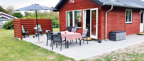 Un edificio rojo de madera con un patio, una mesa con sillas y una parrilla de barbacoa.